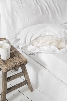 a bed with white linens and a wooden foot stool in front of the bed