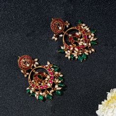 Introducing the Neema Festive Chandbalis by Yamoona, a splendid showcase of heritage style and timeless elegance. These magnificent earrings boast a stud featuring resplendent peacock motifs adorned with ruby red stones and pearls, while emerald green beads gracefully dangle, adding a touch of opulence. A perfect blend of traditional craftsmanship and cultural richness, these chandbalis are destined to elevate your style during festive occasions and special gatherings, leaving an unforgettable i Luxury Traditional Festive Earrings, Luxury Meenakari Jhumkas For Women, Cheap Bollywood Chandbalis For Festive Season, Ruby Emerald Earrings, Luxury Gold Meenakari Chandbalis, Luxury Chandbalis With Intricate Design For Festive Occasions, Luxury Traditional Chandbalis For Festivals, Luxury Ruby Latkans Earrings, Elegant Peacock Design Chandbalis For Festivals