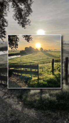 the sun is setting over an open field with a wooden fence and tree in the foreground