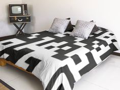 a bed with black and white bedspread sitting next to an old fashioned tv