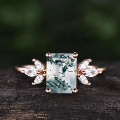 an engagement ring with a green and white stone surrounded by three diamonds on top of a piece of wood