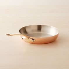 an empty frying pan sitting on top of a wooden table next to a spoon