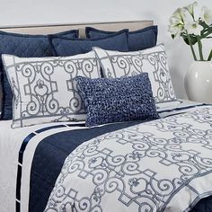 a bed with blue and white comforters, pillows and flowers in a vase next to it