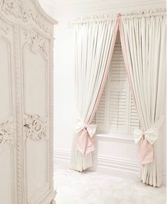 a bedroom with white walls and curtains, pink bows on the window sill, and an ornate armoire