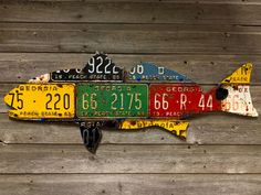 a fish made out of license plates hanging on a wooden planked wall with wood boards