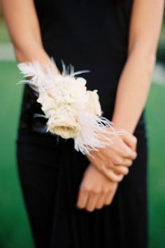 a close up of a person wearing a black dress holding a white flower and feather