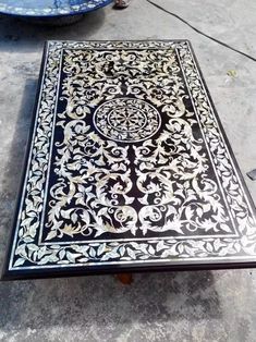 an intricately designed coffee table sitting on the ground next to a potted plant