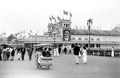 an old black and white photo of people walking on a boardwalk