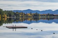 a dock in the middle of a lake with mountains in the background and trees around it