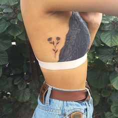 a woman with a tattoo on her back is standing in front of some leaves and flowers