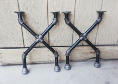 two metal candlesticks sitting next to each other on the ground in front of a wall