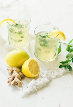 two glasses filled with lemonade next to sliced lemons and ginger on a white cloth