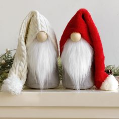 two white and red gnomes sitting on top of a mantle