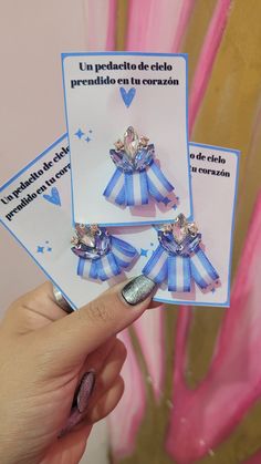 a person holding up two small blue and white bow brooches on top of each other