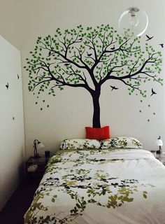 a bed room with a neatly made bed and a tree painted on the wall