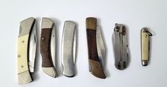 five different types of knives lined up on a white surface with one knife in the middle