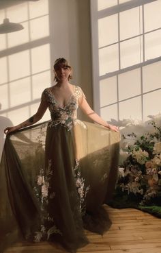 a woman standing in front of a window wearing a long dress with flowers on it