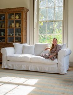 a woman sitting on a white couch in front of a window