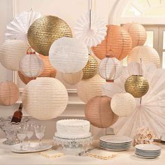 a table topped with lots of white and gold paper lanterns hanging from the ceiling above it