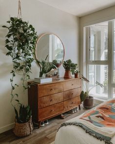 a bedroom with a bed, dresser and plants