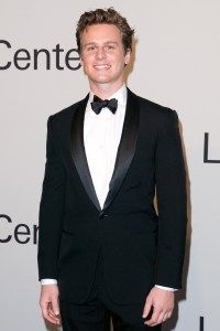 a man in a tuxedo and bow tie standing on the red carpet at an event