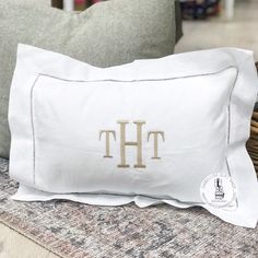 a white pillow with the letter th on it sitting next to a wicker basket