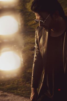 a man in black leather jacket standing next to a wall with three lights on it