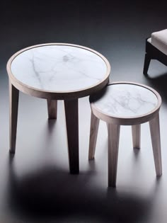 two tables with white marble top sitting next to each other on a black flooring