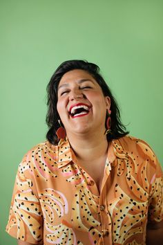 a woman laughing while sitting in front of a green wall with her eyes closed and mouth wide open