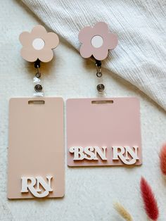 two pink tags with the letters rnn and r on them sitting next to some feathers