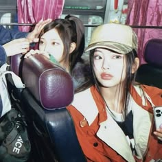 two people sitting on a bus one is brushing her hair and the other is holding a cell phone