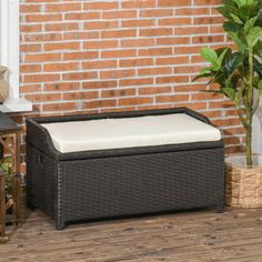 an outdoor storage box sitting on the ground next to a brick wall and potted plant