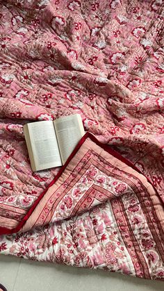 an open book laying on top of a pink and red quilted bed coverlet