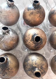 twelve old metal vases sitting on top of a white tableclothed surface with holes in them