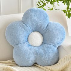 a blue flower shaped pillow sitting on top of a white chair next to a potted plant