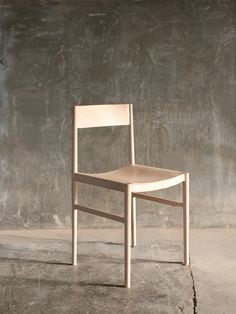 a wooden chair sitting on top of a cement floor next to a gray concrete wall