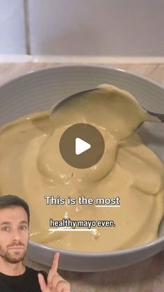 a man holding a spoon in front of a bowl filled with mayonnaise sauce