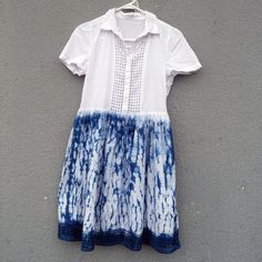 a blue and white dress hanging on a clothes line against a gray wall with a button up shirt underneath it