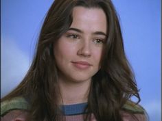 a close up of a person wearing a sweater and smiling at the camera with a blue background