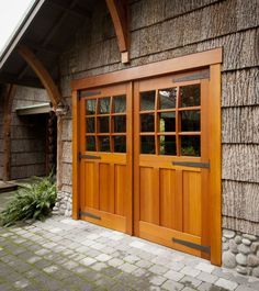 two wooden doors on the side of a building with brick walkway and stone pavers