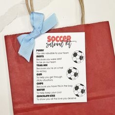 a soccer survival kit is hanging on a red paper bag with a blue ribbon around it