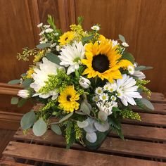 a bouquet of sunflowers and greenery in a green vase on a wooden bench