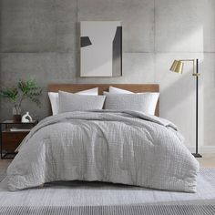 a bed with grey linens and white pillows in a room next to a lamp