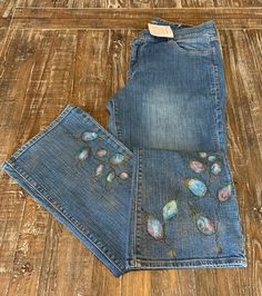 two pairs of blue jeans with flowers on them sitting on a wooden floor next to each other