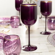 purple wine glasses are sitting on a table next to other glassware and decor items