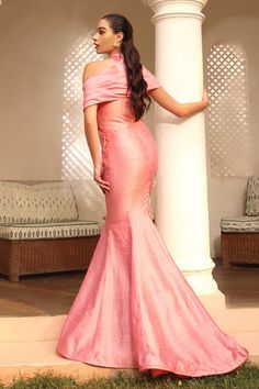 a woman in a pink dress standing next to a white pillar and looking off into the distance