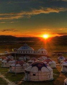 the sun is setting over several yurts in an open field