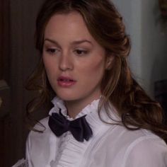 a woman wearing a white shirt with a black bow tie on her neck and long brown hair