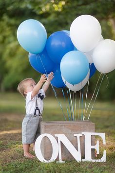 a little boy holding onto some blue and white balloons with the word one on it