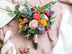 a bridal bouquet laying on top of a bed next to an envelope and napkin